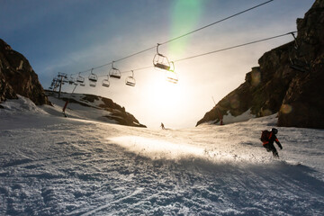 A man skiing down a slope skids in front of the camera as he passes under a chair lift in backlit