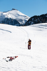 An unrecognizable female skier consults her mobile in the middle of a ski slope with some skis in the foreground