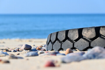 Fototapeta na wymiar Discarded worn car tire. Clogging of the sea coast