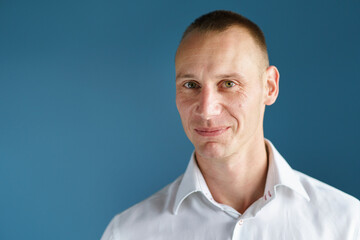 Fototapeta premium Front view close up portrait of male adult caucasian man with short blonde hair and green eyes in front of blue background looking to the camera smiling with copy space