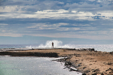 Silhouette of a young girl fishing off Olawalu Landing on Maui with an explosive wave crashing.