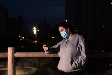 Woman with protective face mask checking her smart phone in a park.