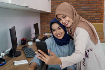 a portrait of a beautiful Muslim woman who is very happy with her partner and selfie while working at office studio