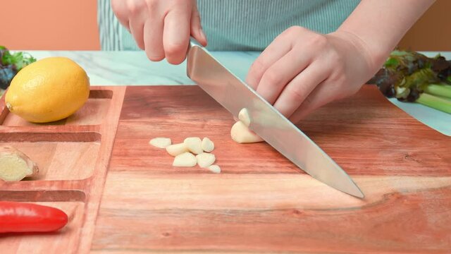 A close-up look of chopping garlic cloves on a wooden cutting board in 4K. Concept of cutting garlic with a chef knife as an ingredient for seared Tuna.