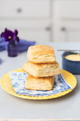Three Homemade Biscuits Stacked on a Yellow Plate with Butter in a Blue Bowl on a White Kitchen Countertop