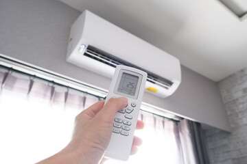 Man's hand using remote control open The air conditioner is cooled to 25 degrees Celsius in his bedroom. Health concepts and energy savings