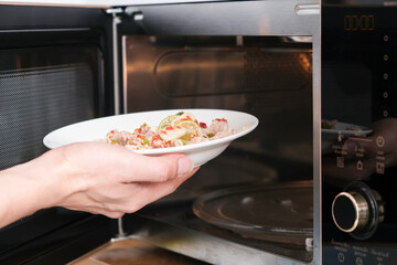 A housewife steaming fish in a microwave oven for a family dinner. She prepares it by putting fish dishes in the microwave and then serving healthy food. Cooking ideas