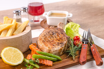 The delicious grilled ribeye beef steak on the wooden cutting board with french fries and fresh vegetables salad.