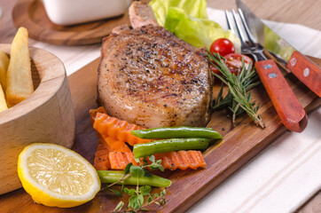 The delicious grilled ribeye beef steak on the wooden cutting board with french fries and fresh vegetables salad.