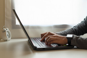 Close-up of a man working or typing on a laptop at a desk in a warm, warm home