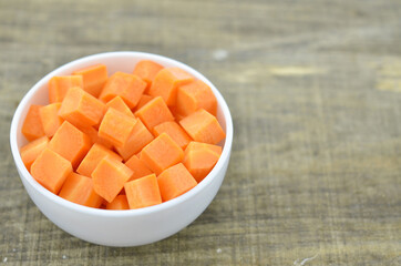 cuts cubes of carrot in bowl on wooden background