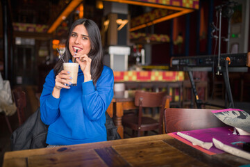 Portrait of pretty brunette in a cafe. Enjoying latte and looking at camera.