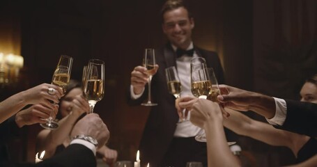 Handsome man making a toast with friends at party. Friends sitting at a table, toasting with wine and enjoying dinner together.
