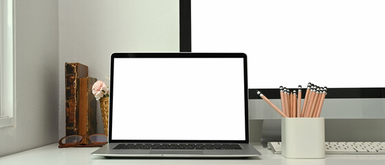 Modern workspace with blank screen laptop, pencils and book on white table.