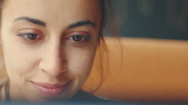 extreme closeup young pretty woman joyfuly looking at laptop screen and listening music from outside and sways to the beat of the music. dark brown womans eyes reflets laptop