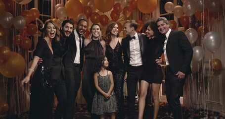 Diverse group of people with a cute girl standing together looking at camera and smiling. Rich people posing for a group portrait on new years eve party.
