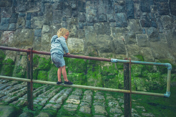 Preschooler playing by railing on the beach in autumn
