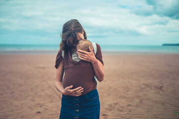 Young mother standing on the beach with her baby in sling