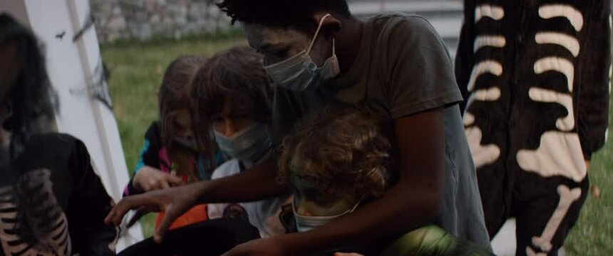 Group of trick-or-treating kids wearing face masks receiving candies from home owners. Halloween celebration during virus pandemic . Shot on RED Cinema camera with 2x Anamorphic lens