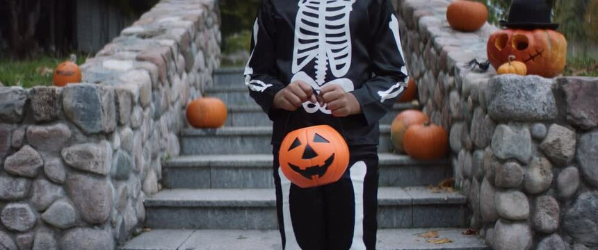 Unrecognizable kid wearing skeleton costume posing with jack-o-lantern shaped basket during Halloween. Shot on RED Cinema camera with 2x Anamorphic lens
