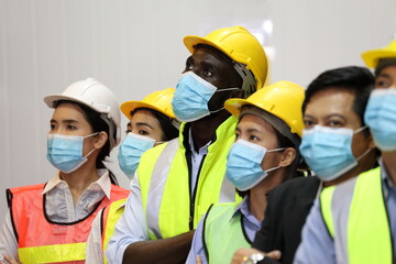 Manager and the rest of the engineering team standing together in the factory wearing facial mask...