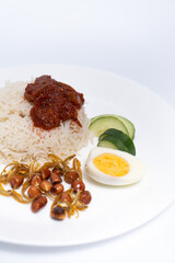 A close-up of Nasi Lemak-Malaysian cuisine. A fragrant rice dish cooked in coconut milk and pandan leaf commonly found in Malaysia. Served with sambal, anchovies, peanut, and cucumber.