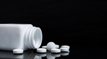 White pills and medicine bottles on black background.