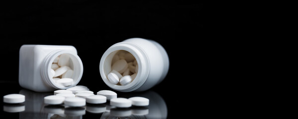 White pills and medicine bottles on black background.