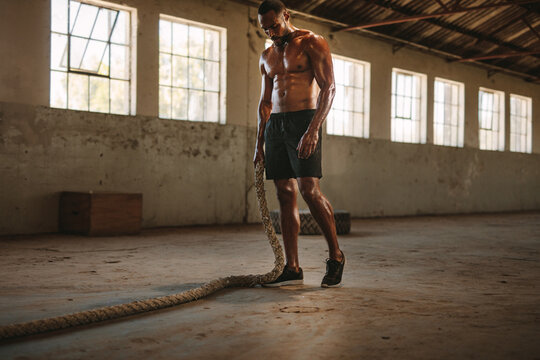 Muscular man in fitness studio with battle rope