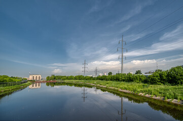 A small river, on the banks of the river there are high-voltage line towers