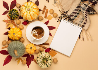 Autumn composition with cup of coffee, pumpkins, apples, nuts and cinnamons on pastel beige background.