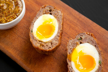 Homemade Scotch Eggs on a rustic wooden board on a black background, close-up.