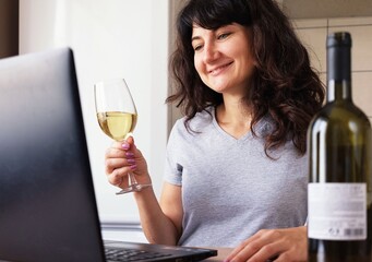 The girl communicates with via video communication and holds a glass of wine in her hand.