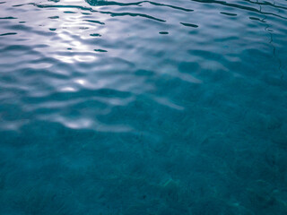 Fototapeta premium Surface of a crystal clear turquoise water. Sandy sea ground. Sun light reflecting above waves. Blue natural background
