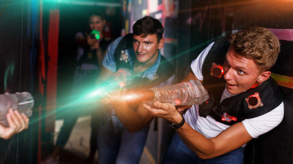 Portrait of positive friends standing with laser guns during laser tag game in dark room