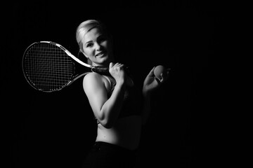 Fototapeta na wymiar Young female tennis player posing with racket on black background