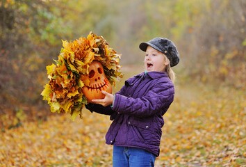 child-a little girl in a cap and purple jacket screams feigning fright and holds a pumpkin Jack's...