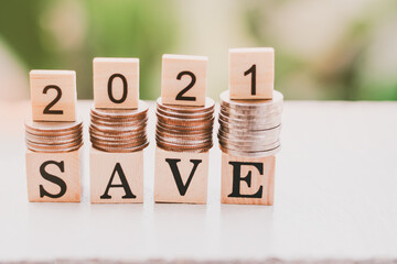 Coins stacks and Text of save and 2021 number written on wooden blocks with stack of coins,Nature day light background, Business and Saving money for new life new year concept, Selective focus.