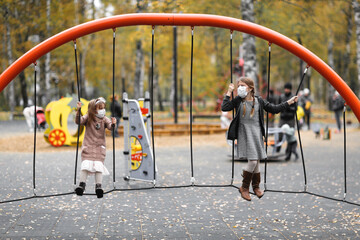 children in the playground in masks, girls friends play through the net in the park, protection from the virus, social distance and friendship, quarantine and restrictions