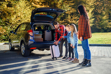 Joyful lovely young family loading the auto's trunk by carton boxes and suitcases while relocating...