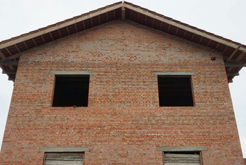 large unfinished house made of brown and red bricks with empty windows against a gray sky
