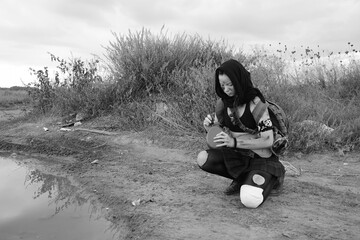 Post apocalyptic survivor. Young slim girl warrior with weapon outdoors, in shabby clothes.