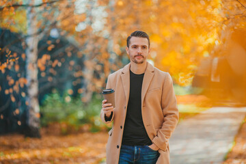 Young man drinking coffee in autumn park outdoors
