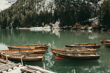 Wooden rowing boats on Braies lake in Dolomites during autumn or winter season. Emerald water, green pine trees with snow in the top of mountains. Desolate, wild, low-season concept.