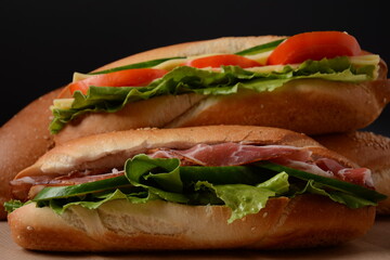 Fresh submarine sandwiches with bacon, cheese,  tomatoes, lettuce, cucumbers and onions on dark background