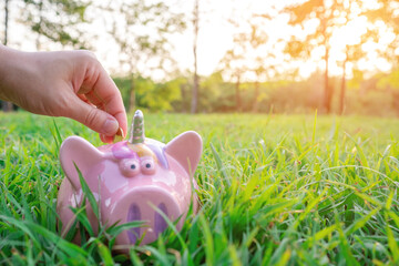 Closeup of hand putting coin in piggy bank with nature background. Business Banking and Financial...