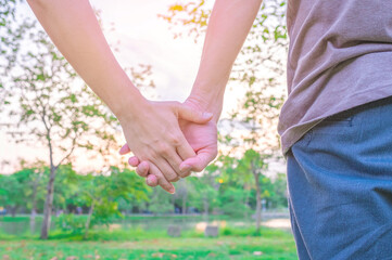 Closeup woman holding man hand while leading him on nature outdoor. Couple in park on sunset.