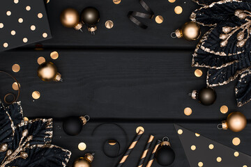 Luxury black and gold Christmas frame on wooden background. Golden and black baubles and other Christmas decorative elements on dark wood planks with copy space. New Year flat lay.