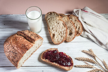 A glass of milk, sliced rustic bread and jam, on a white wooden board. Healthy food and farming concept