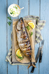Traditional Australian barbecue bonito fisch with tzatziki and lemon slices offered as top view on a rustic wooden board